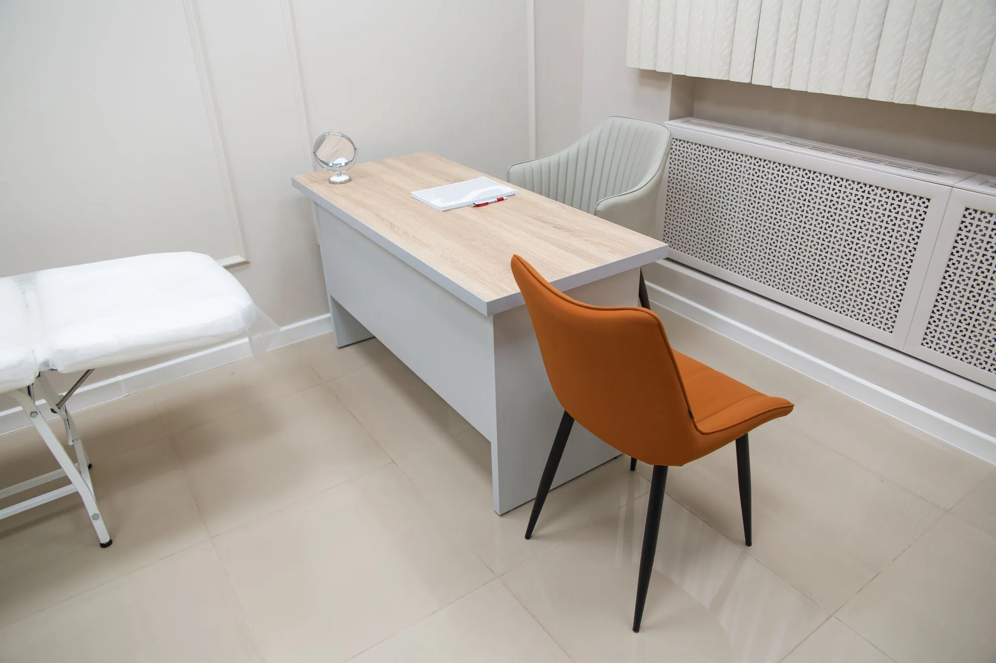 Clean clinic consultation room with desk and treatment bed